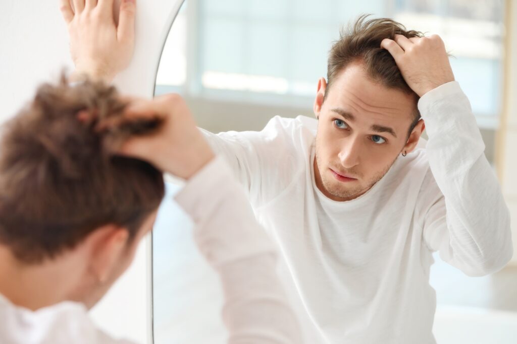 Young,Man,With,Hair,Loss,Problem,Looking,In,Mirror,At PRP Hair Restoration Sugar Land TX