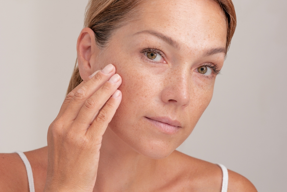 Anxious woman looks in the mirror in Sugar Land, thinking of laser pigment removal for her freckles and sun spots